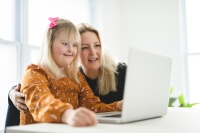 Blond little girl with down syndrome sitting next to her mother in front of a laptop