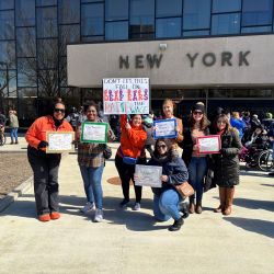 care design New York team members holding signs out front of the New York State building